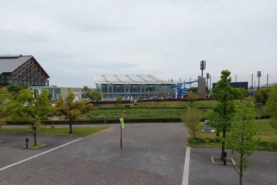 緑地の向こうに見えるアクアパレットまつやまの建物と屋外スライダー